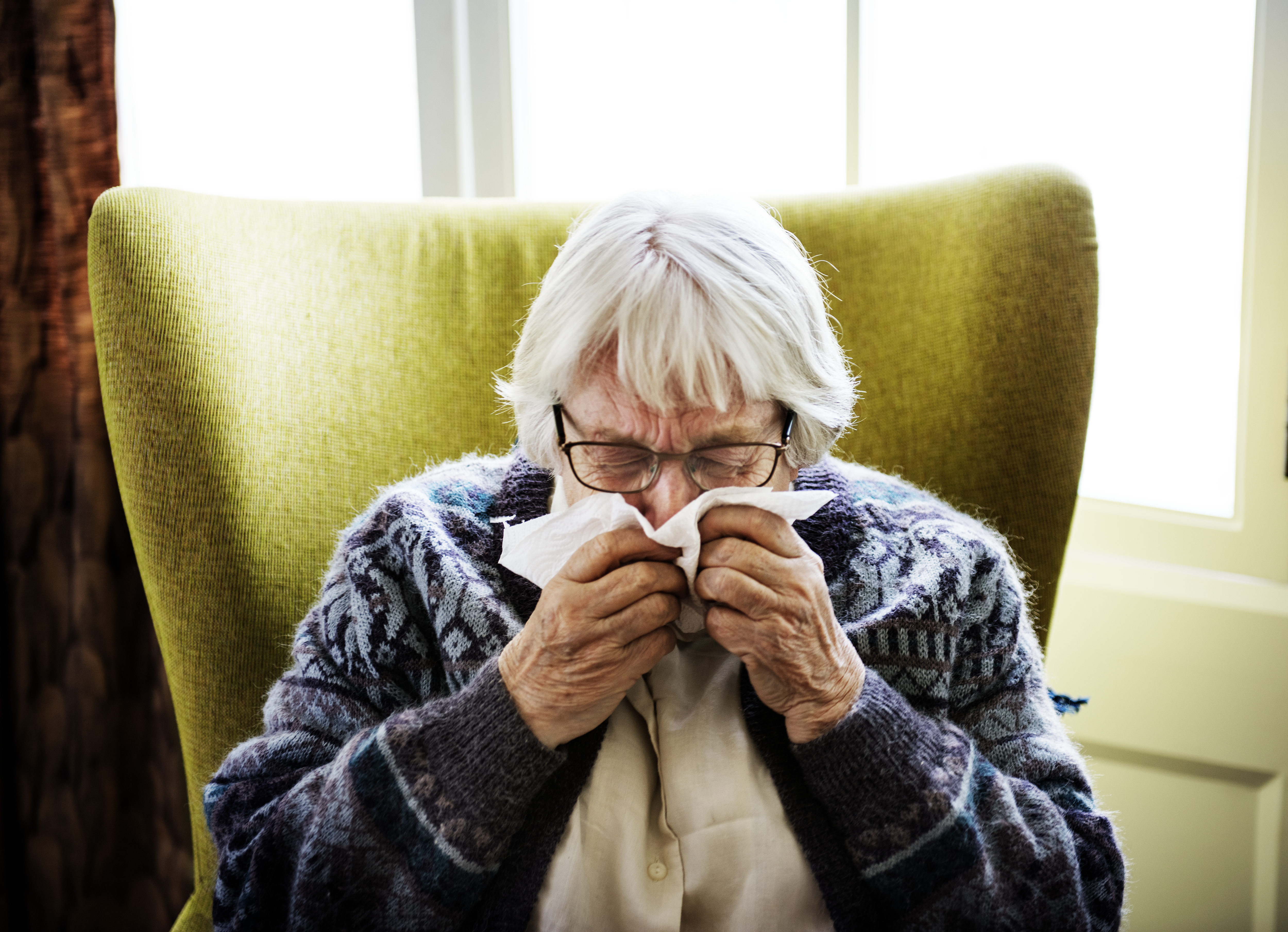 Photo of elderly woman sneezing into a tissue